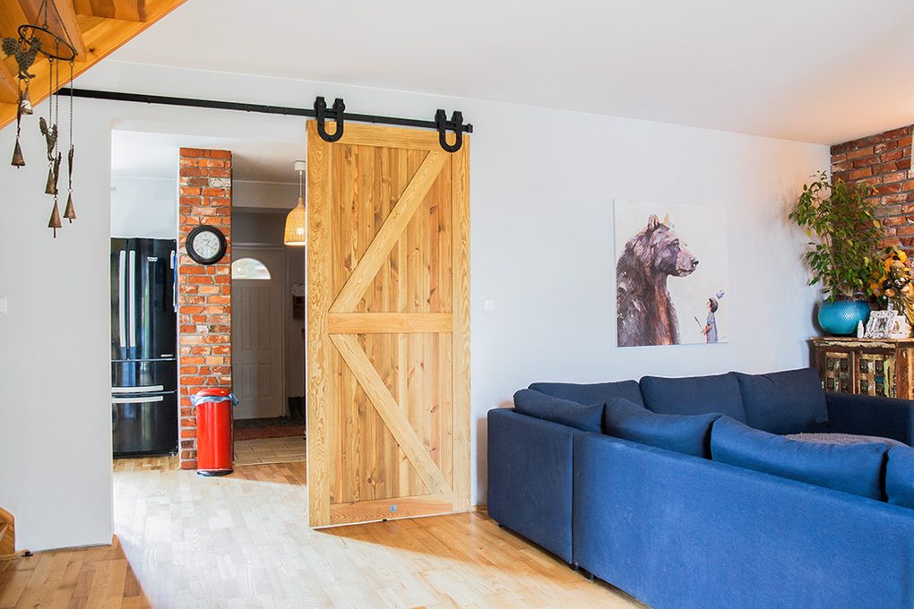 rustikale Holztür, Schiebetür aus gebürstetem Holz, barn door, Schiebetür mit einem Hufeisen, Schiebetür zur Küche, großes blaues Sofa im Wohnzimmer, Ziegel an der Wand