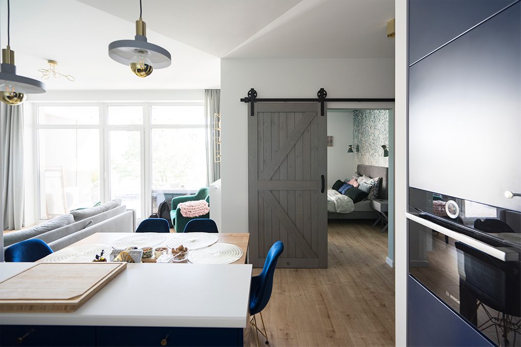 Holzschiebetüren, Scheunen-Schiebetüren, Schiebetür holz grau, goldene Accessoires im Innenraum, modernes Interieur, Durchgang zwischen Wohn- und Schlafzimmer, Eingang zum Schlafzimmer, klare Farben im Innenraum, blaue Esszimmerstühle, offener Raum