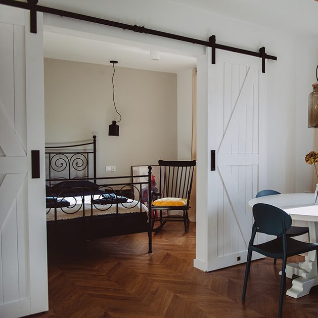 moderner Retro-Stil, Mietwohnungen Wroclaw, Doppelschiebetüren, weiße Schiebetüren, barn door, offener Raum, Doppeltür für Schlafzimmer, Retroschlafzimmer, Schaukelstuhl im Schlafzimmer