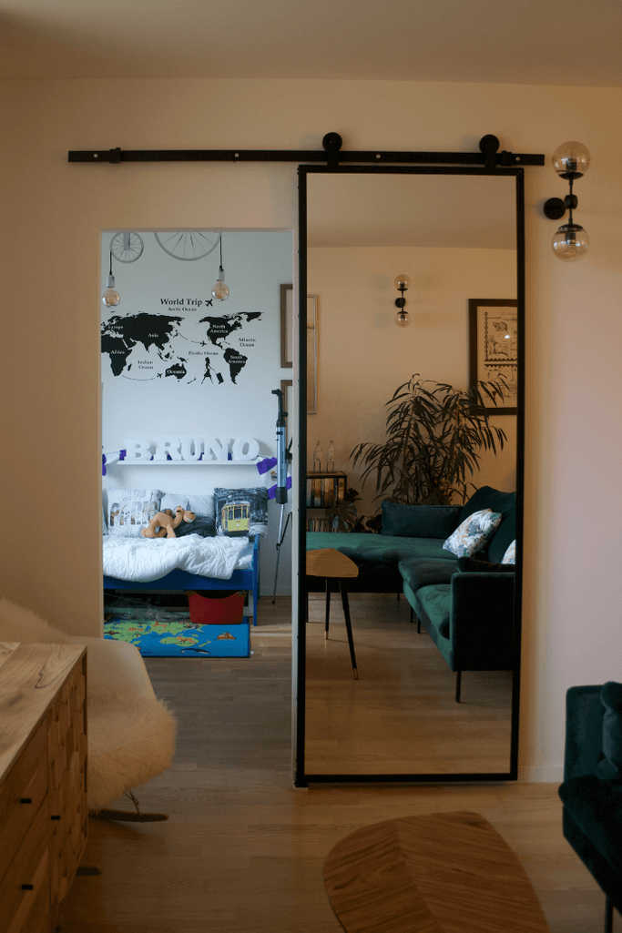 Schiebetür mit Spiegel, Tür mit Spiegel in einem Metallrahmen, Schiebetür in einem modernen Interieur, Sofa im skandinavischen Stil, grünes Sofa, Metal Wandlampen