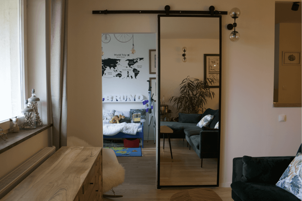 Schiebetür mit Spiegel, Tür mit Spiegel in einem Metallrahmen, Schiebetür in einem modernen Interieur, Sofa im skandinavischen Stil, grünes Sofa, Metal Wandlampen