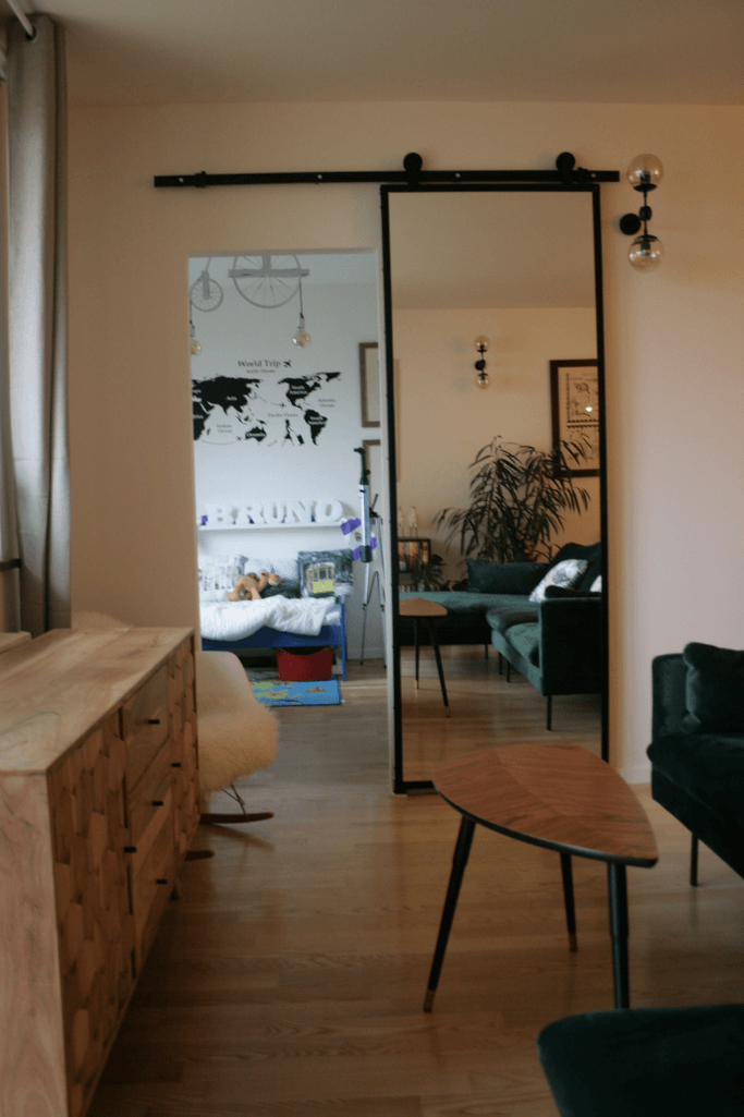 Schiebetür mit Spiegel, Tür mit Spiegel in einem Metallrahmen, Schiebetür in einem modernen Interieur, grünes Sofa, Kommode im modernen Stil, Tisch im skandinavischen Stil