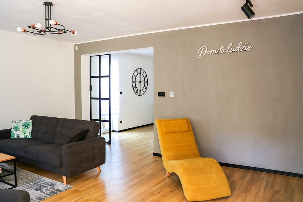 offenes Wohnzimmer, graues Sofa im Wohnzimmer, Industrielampe im Wohnzimmer, gelber Sessel für das Wohnzimmer, graue Wand im Wohnzimmer, Wohnzimmer offen zum Esszimmer, Metalltür mit Glas, Schiebetür mit Glas, Tür im Loft-Stil, Leuchtreklame an der Wand, Neondekorationen
