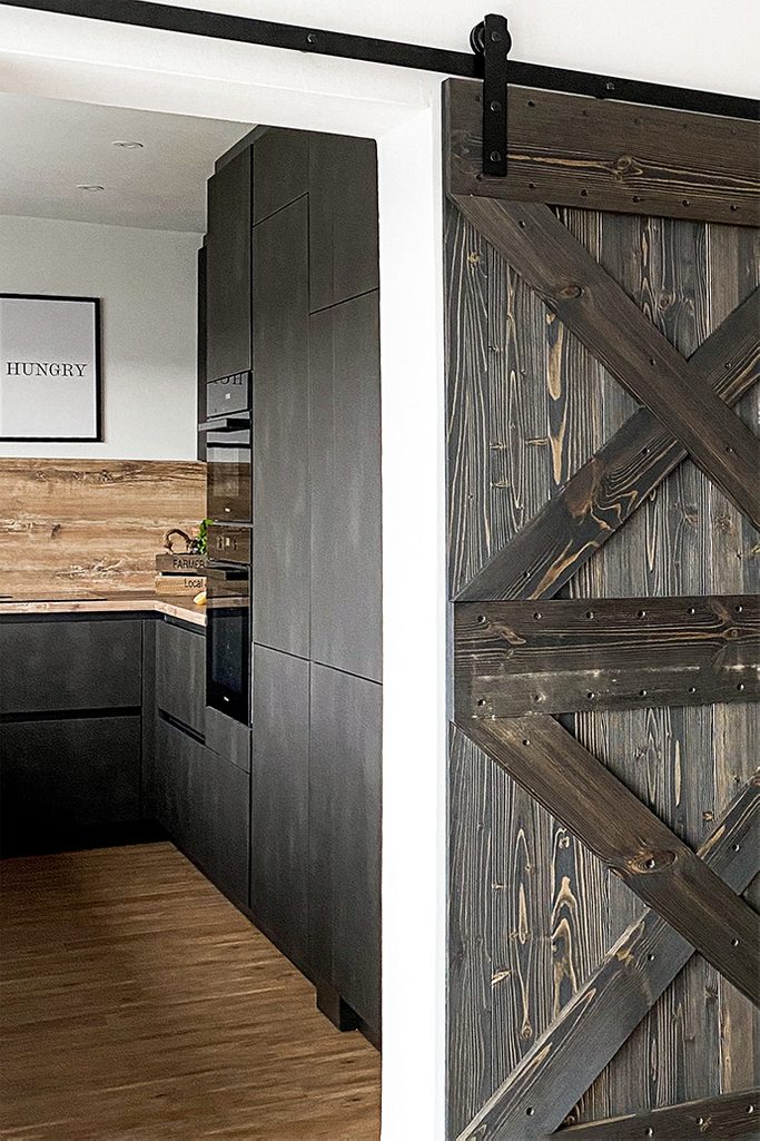 Holz und Metall im Esszimmer, dunkelbraune Einbauküche, dunkle Möbel in der Küche, Holzschiebetür, Schiebesystem, Holztür zur Küche