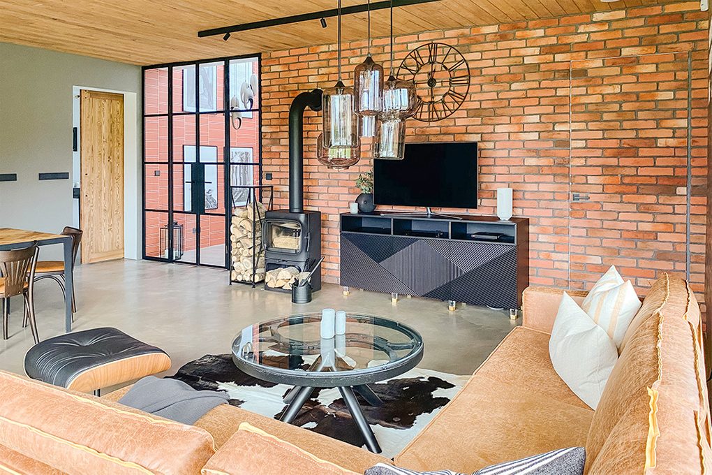 Wohnzimmer im Industrie loft stil, Mikrozement Boden, Holzdecke, schwarze Metallelemente, schwarzer Kamin im Wohnzimmer, Glas- und Stahllampe, Couchtisch aus Glas, Backsteinmauer im Wohnzimmer