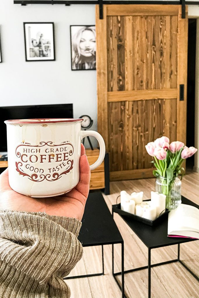 Schiebetüren in einer kleinen Wohnung, Satz von zwei schwarzen Couchtischen, Holzschiebetür im Wohnzimmer, schwarz-weiße Plakate an der Wand, Kaffeetasse