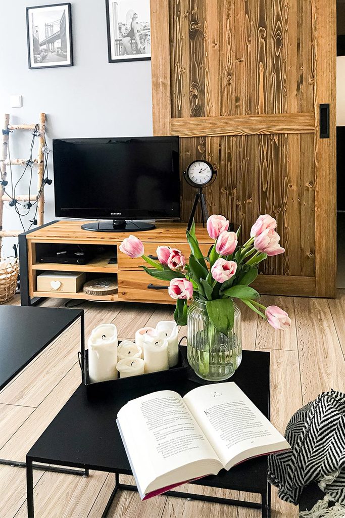 Schiebetüren in einer kleinen Wohnung, schwarzer Metall-Couchtisch, Holzschiebetür mit schwarzem Griff, TV-Schrank aus Stahl und Holz, dekorative Kerzen und Tulpen auf dem Couchtisch