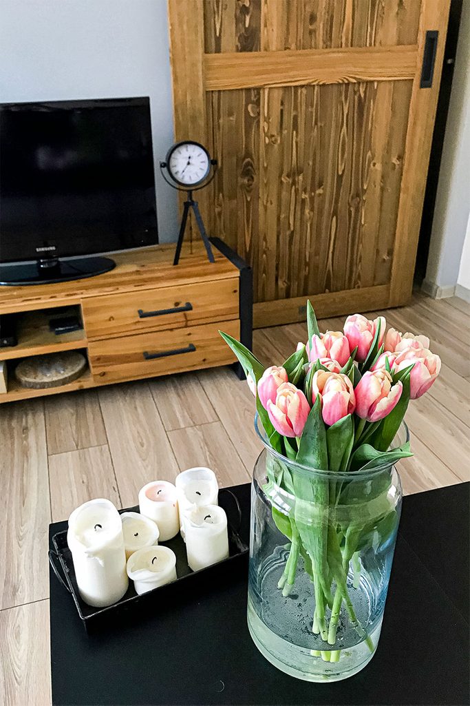 Schiebetüren in einer kleinen Wohnung, Holzschiebetür mit schwarzem Griff, Holz Fernsehschrank, dekorative Metall Uhr auf Holzschrank