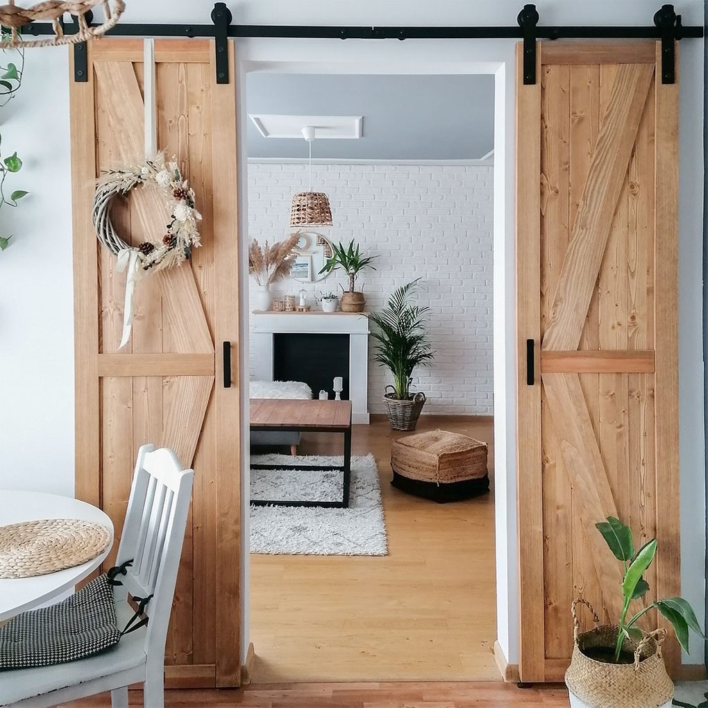 schmale Schiebetür, schmale Holztür am Schiebesystem, schmale Tür in der Küche, Schiebetür zwischen Küche und Wohnzimmer, Wohnung im Boho-Stil, Kranz an der Holztür, weiße Backsteinwand im Wohnzimmer