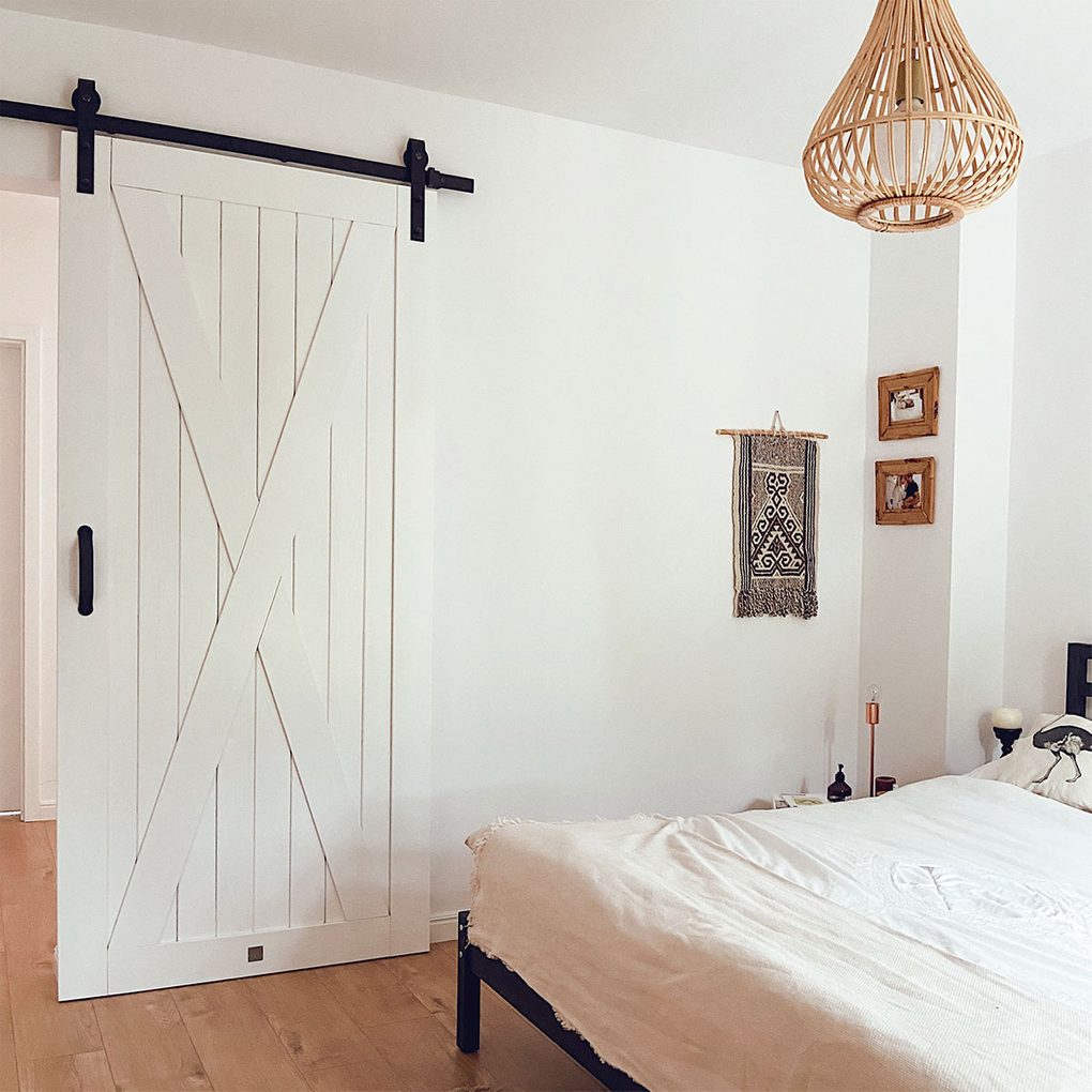 Weiße Massivholz-Schiebetür im Eingang zum natürlichen Schlafzimmer, weiße Wände im Schlafzimmer, Bambus-Pendelleuchte, natürliche Boho-Dekorationen an der weißen Wand