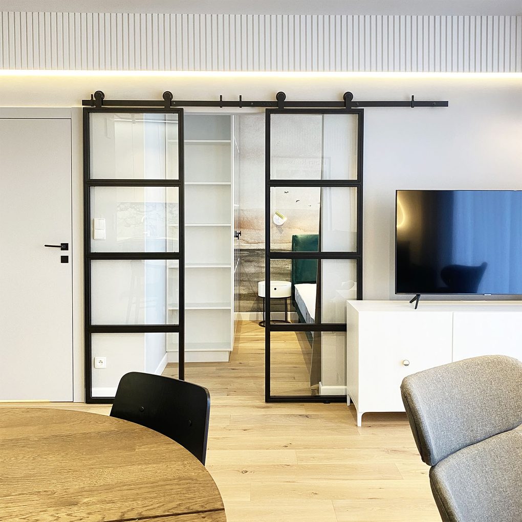 Doppelglasschiebetüren in einem Metallrahmen, die Wohn- und Schlafzimmer in einer modernen Wohnung trennen, weiße Wände und heller Boden
