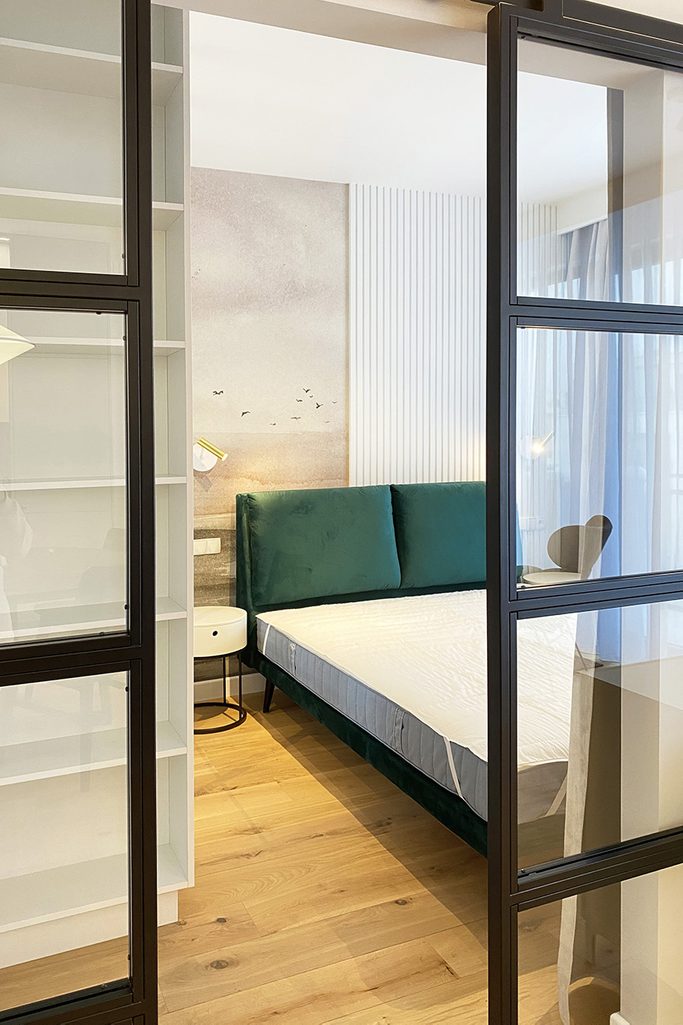 doppelt, Metallschiebetür mit Glas im Eingang zum Schlafzimmer, moderne Wohnung, geradliniger Stuck im Schlafzimmer, Bett mit Polsterkopfteil