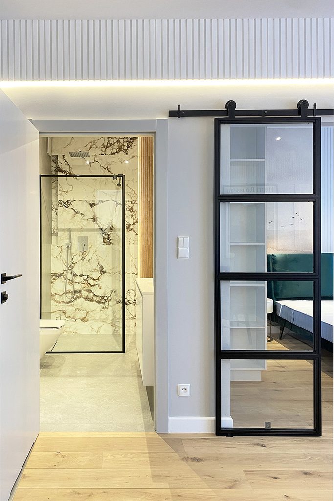 Glasschiebetüren neben dem Eingang zu einem modernen Badezimmer, Badezimmer im minimalistischen Stil, helle Wände und linearer Stuck in einer modernen Wohnung