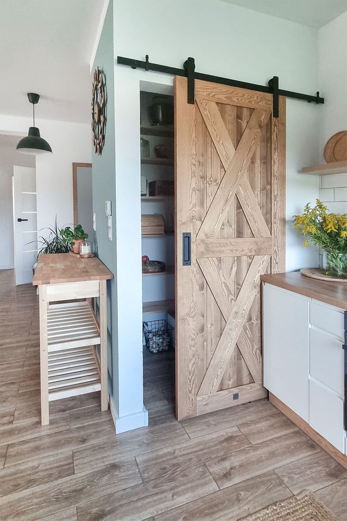 offene Holzschiebetür zu einer kleinen Speisekammer in einer hellen Küche