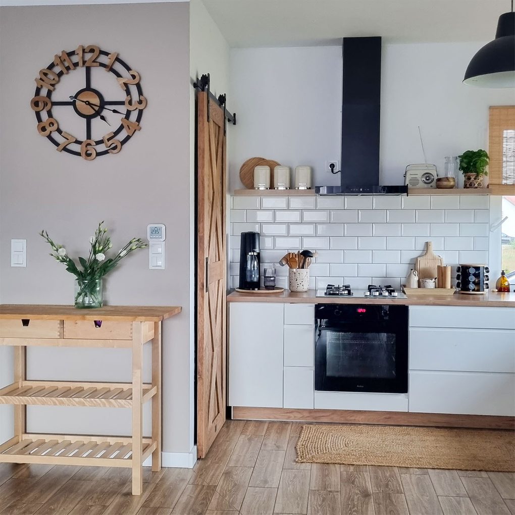 weiße Küchenschränke mit Holzplatte neben der Holztür zur Speisekammer