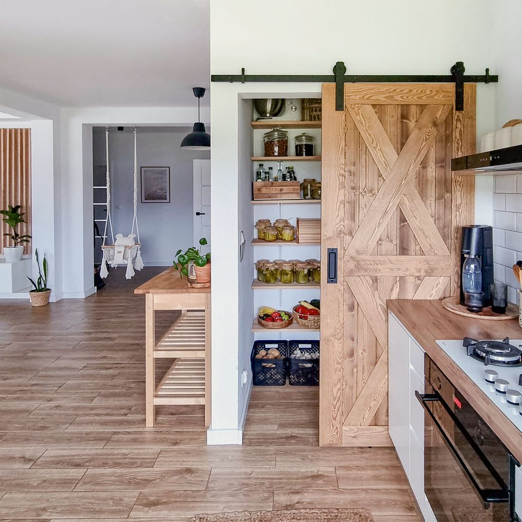 offene Holzschiebetür zu einer kleinen Speisekammer in einer hellen Küche