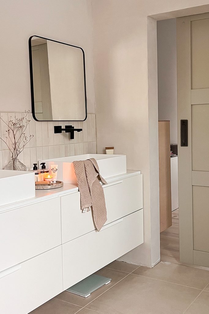 quadratischer Spiegel über einem rechteckigen Waschbecken auf einem weißen Schrank mit großen Schubladen