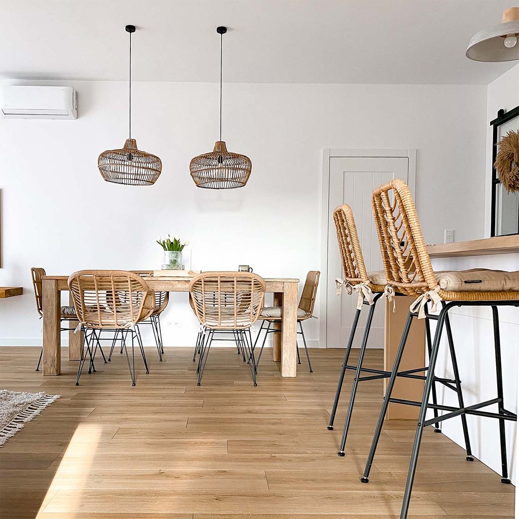 Rattanstühle auf Metallbeinen, Rattanbarhocker und Hängelampen aus Korbgeflecht in einem Wohnzimmer mit weißen Wänden