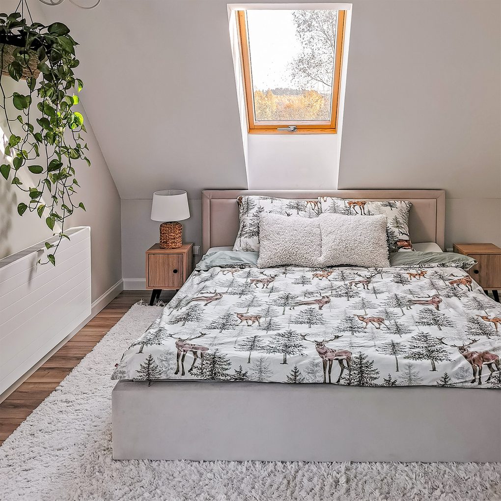 Bettwäsche mit Waldmotiven auf einem Polsterbett mit Kopfteil unter dem Dachfenster